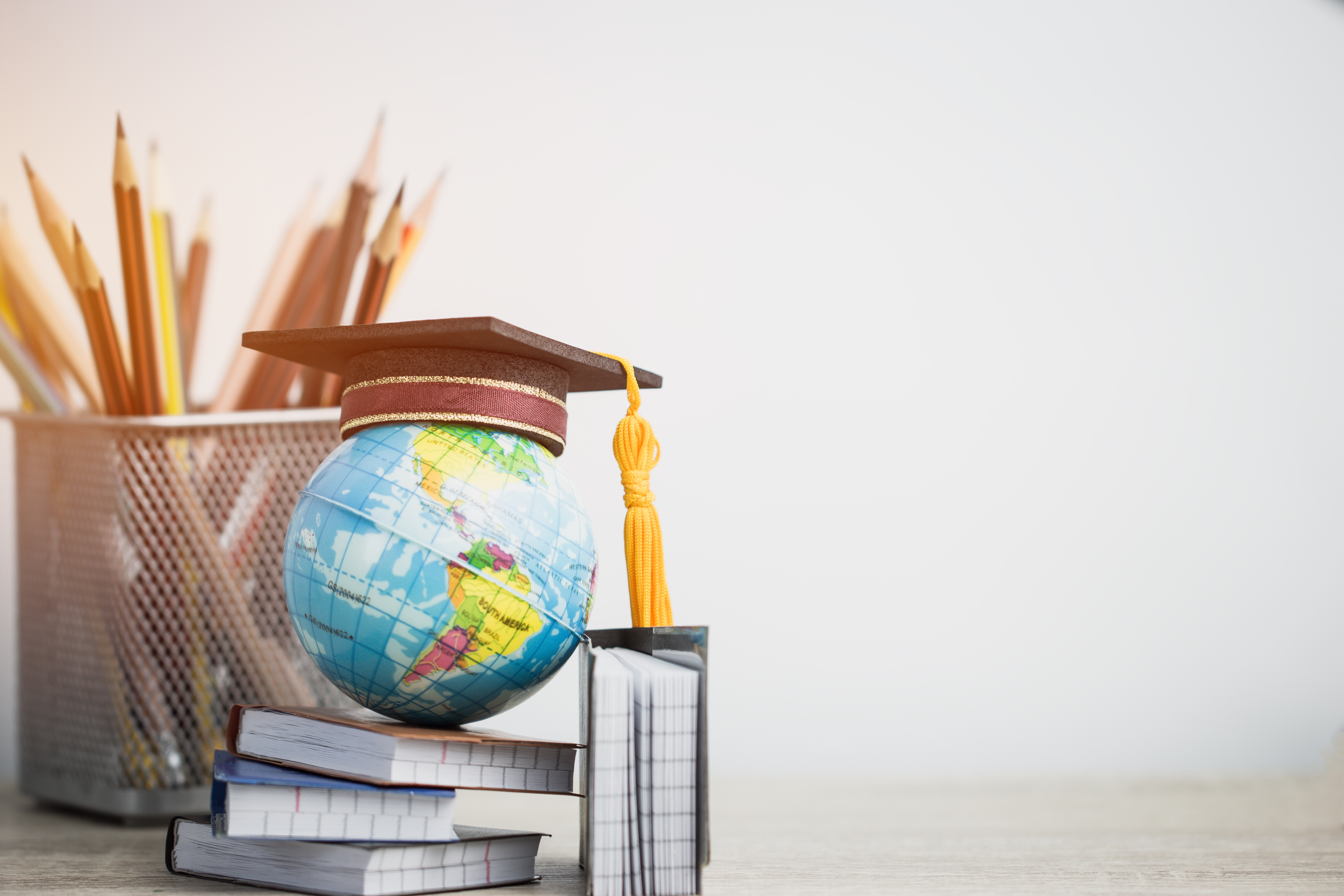 Global education, higher education. Graduation hat on models globe, books with pencils on wood white background.